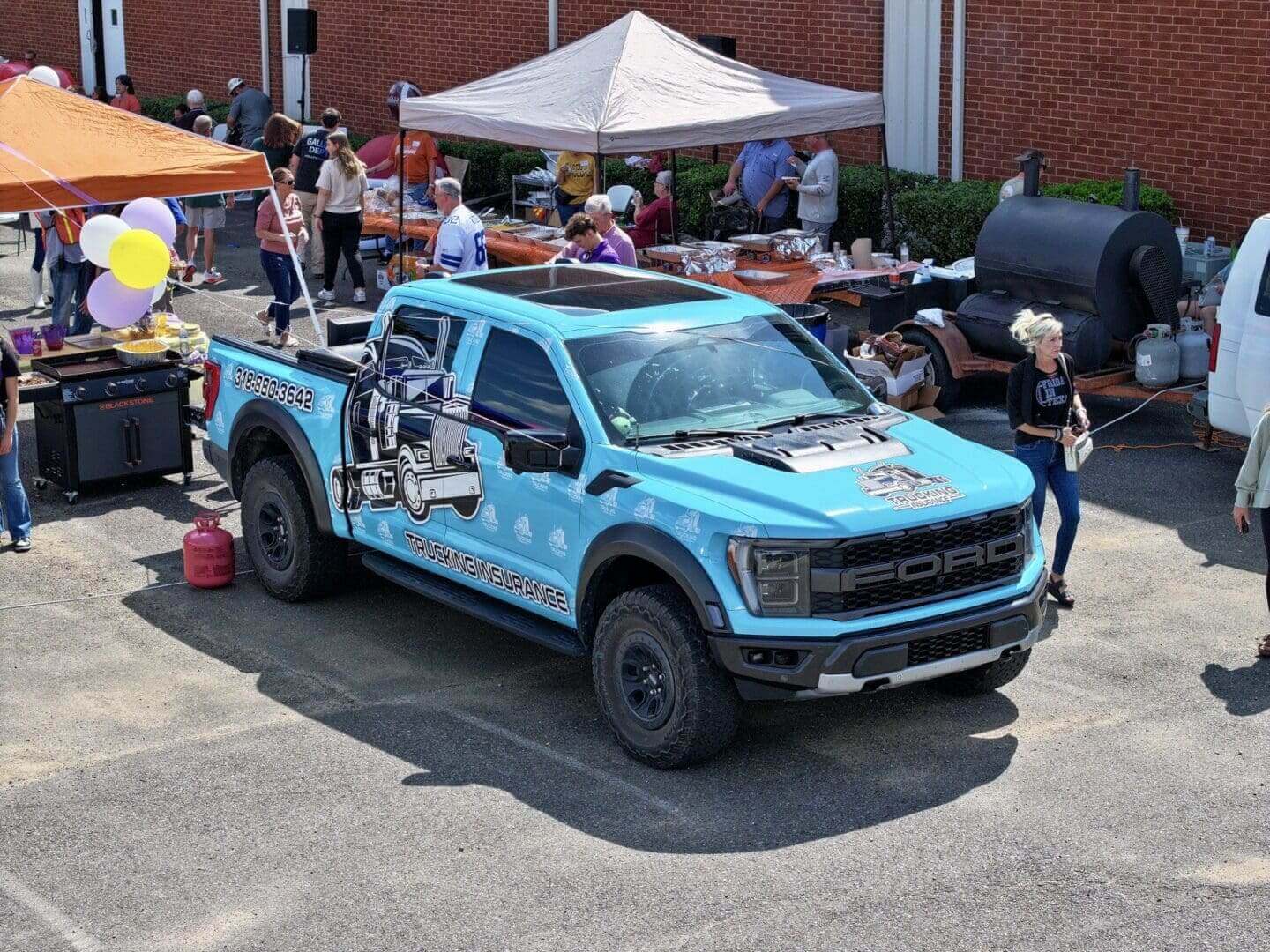 Customized blue truck with exposed engine parts at an outdoor event.