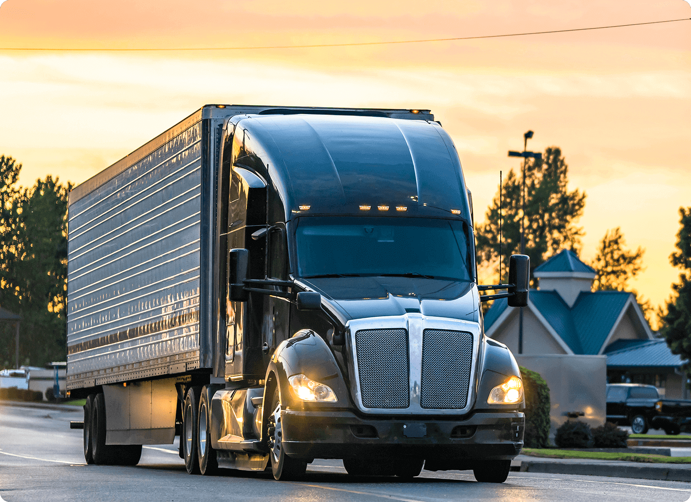 A black semi-truck driving on a highway during sunset.