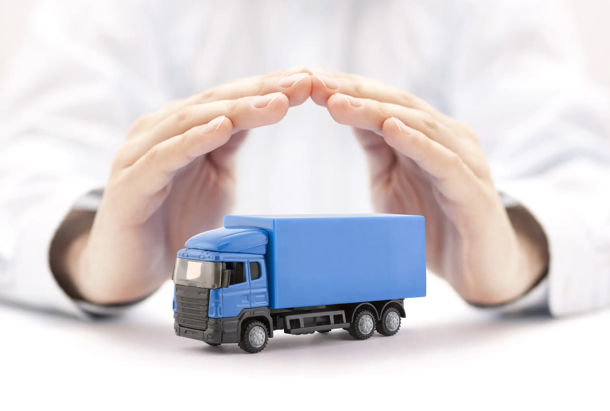 Hands protecting a small blue truck model, symbolizing vehicle insurance or safety.