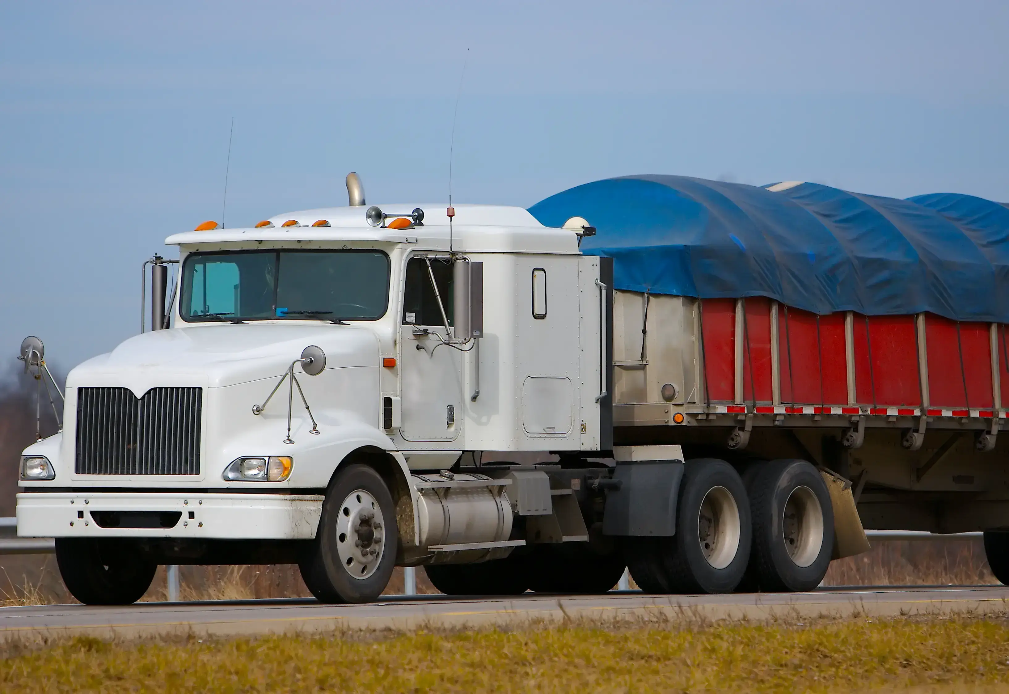 White semi-truck hauling a large covered load on a highway.