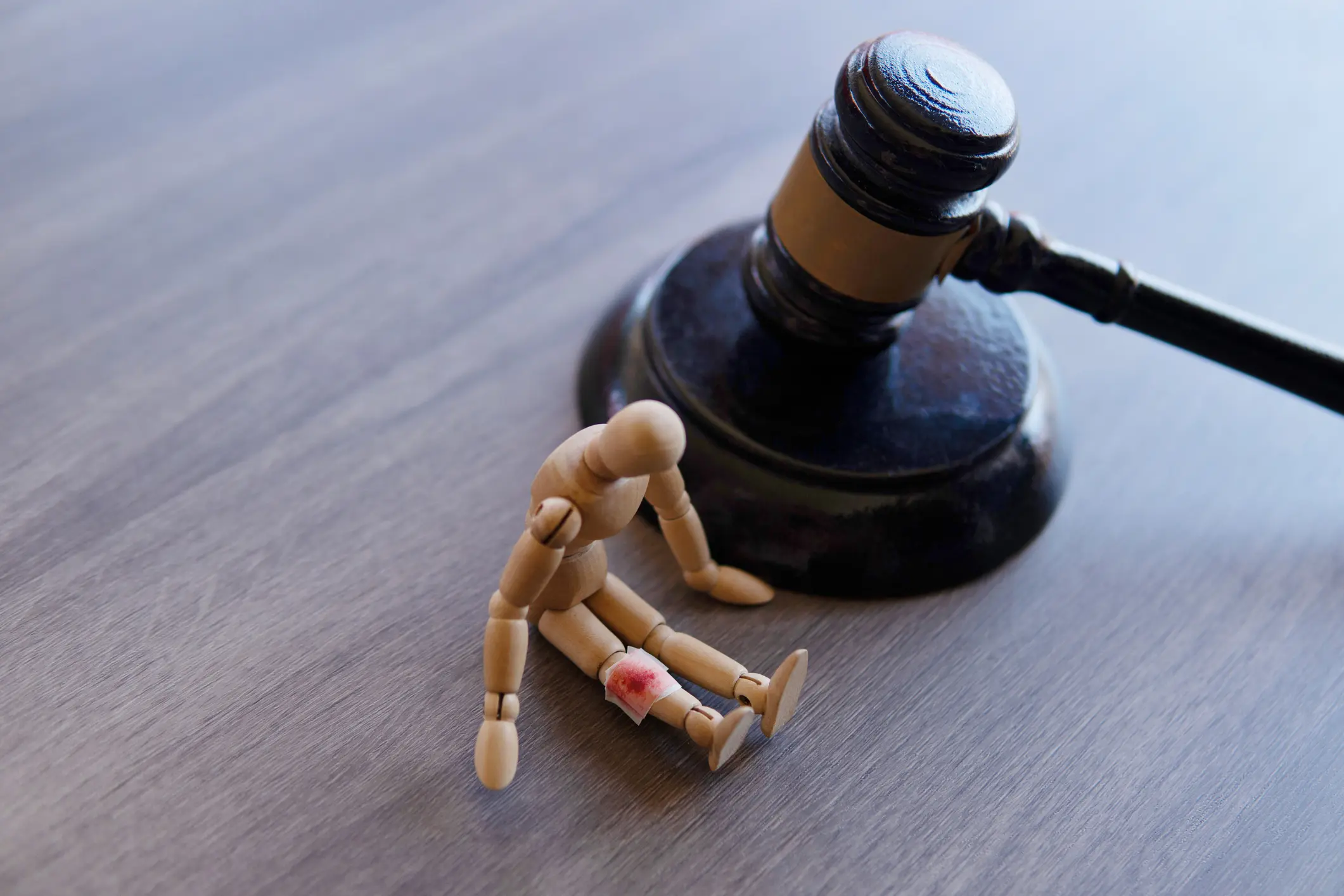 A wooden mannequin with a red wound sits near a judge's gavel.