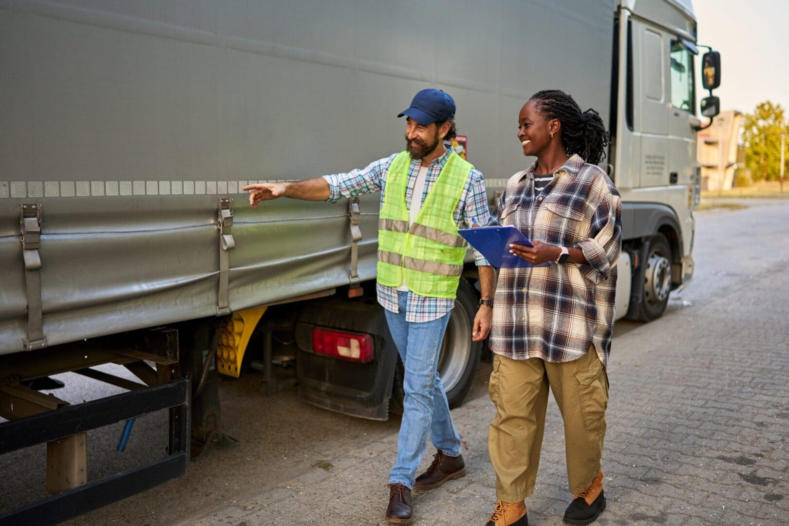 Two men discussing logistics near a delivery truck, one wearing a safety vest.