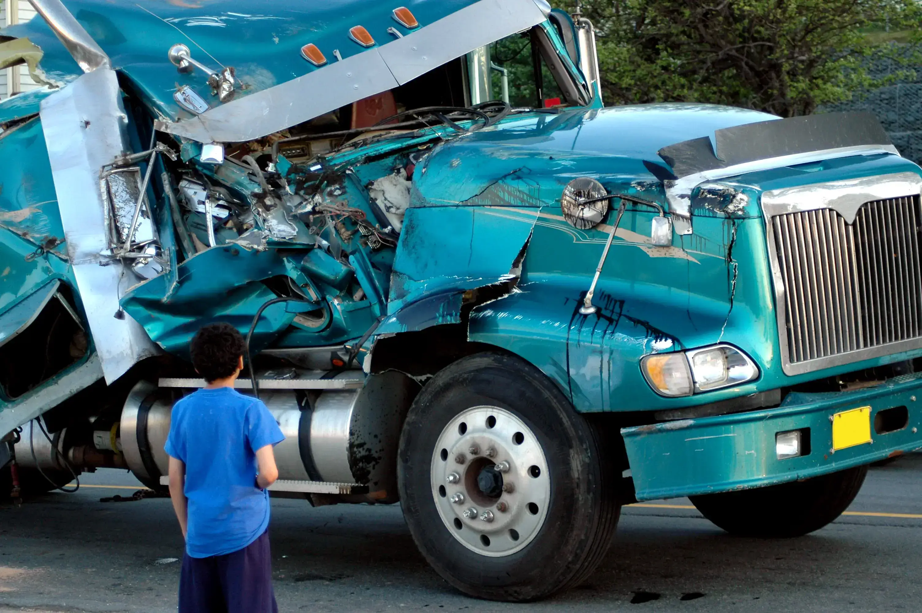 Person observing a heavily damaged blue truck after an accident.